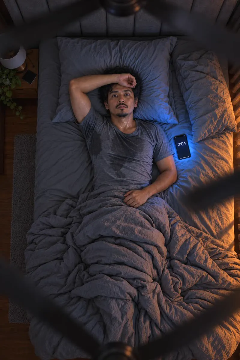 GAMBAR HERO Orang terjaga pukul 2 pagi: berpeluh, kipas laju, cahaya telefon di muka. Bilik malam, tiada aircond.